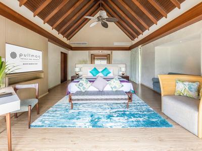 Gemütliches Schlafzimmer mit hohen Holzbalken, modernem Bett und blau-weißem Teppich.