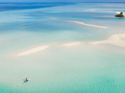 Weites, klares Wasser mit hellem Sand und zwei kleinen Booten, ruhige und helle Farben.