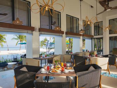 Moderner Speiseraum mit großen Fenstern, Korbstühlen, gedeckten Tischen und Blick auf Palmen.