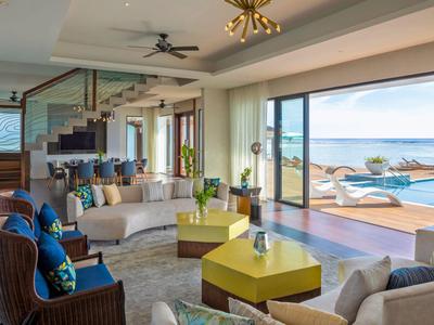 Sala de estar moderna con sofás, mesas amarillas y gran vista al mar a través de puerta corredera de vidrio.