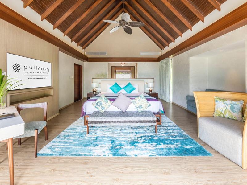 Gemütliches Schlafzimmer mit hohen Holzbalken, modernem Bett und blau-weißem Teppich.