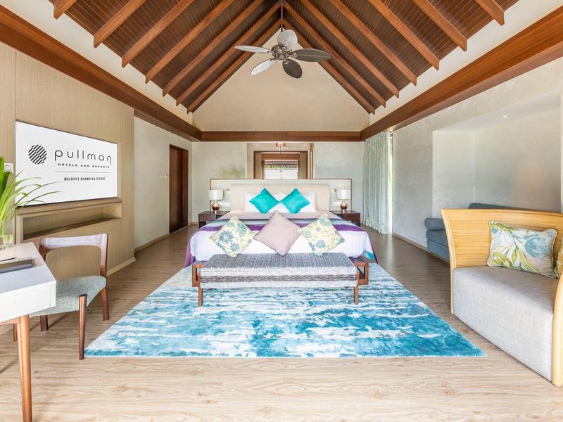 Helles Schlafzimmer mit Holzbalkendecke, großem Bett, blauem Teppich und moderner Einrichtung.