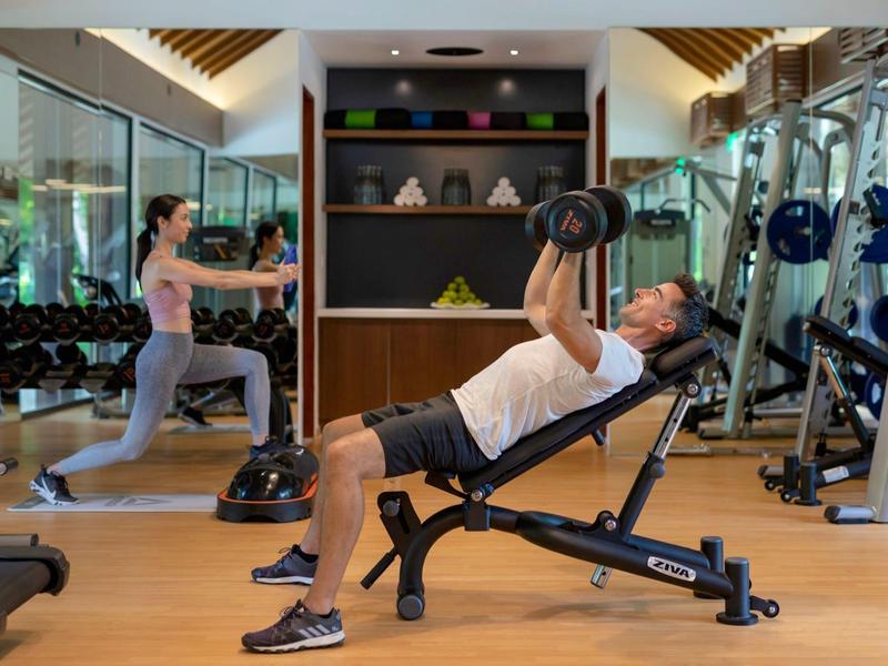 Im Fitnessstudio trainieren zwei Personen mit Hanteln, Umgeben von Spiegeln und Geräten.