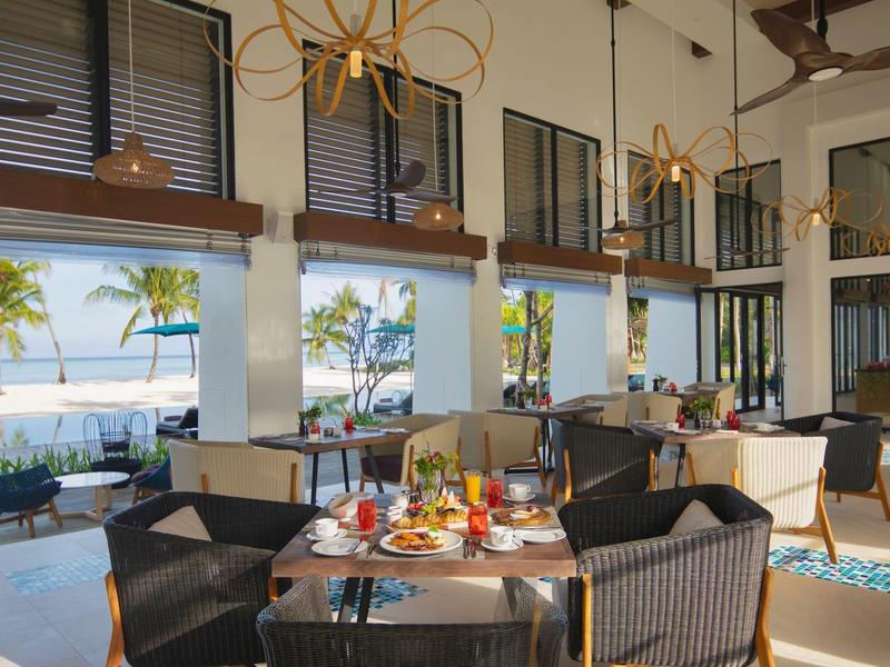 Moderner Speiseraum mit großen Fenstern, Korbstühlen, gedeckten Tischen und Blick auf Palmen.