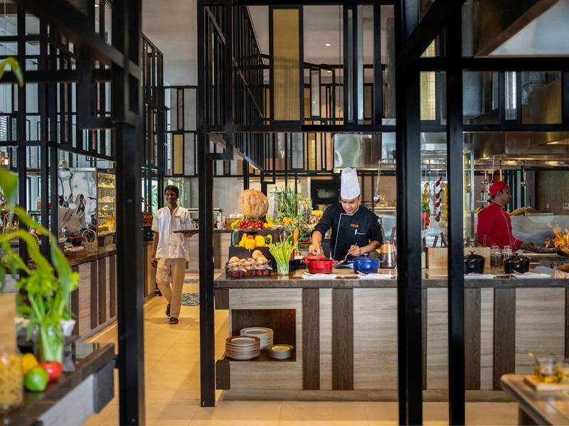 Moderne Restaurantküche mit Koch, frischem Obst, Gemüse und großen Fenstern, viel Holz und Glas.