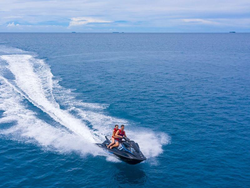 Zwei Personen fahren auf einem schwarzen Jetski über das blaue Meer mit bewölktem Himmel.