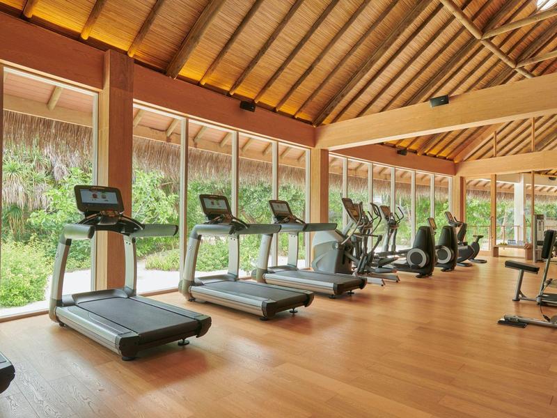 Großer Fitnessraum mit Holzboden und mehreren Laufbändern vor bodentiefen Fenstern.