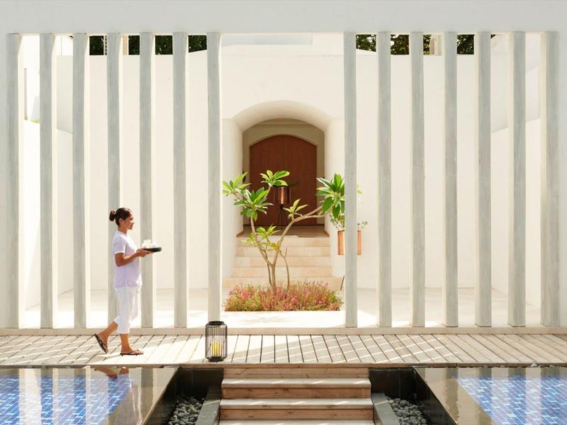 Ein Mann in weißer Kleidung liest neben weißer Säulenstruktur und blauem Wasserbecken.