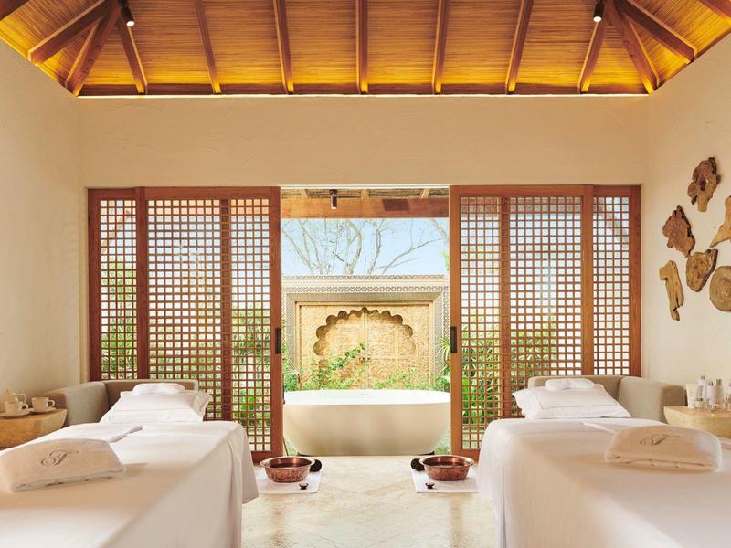 Helles Spa-Zimmer mit zwei Liegen, Holzdecke, großen Fenstern und Blick auf Garten.