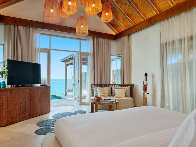 Helles Schlafzimmer mit Holzbalken, großem Bett, TV und Meerblick durch Glastüren.