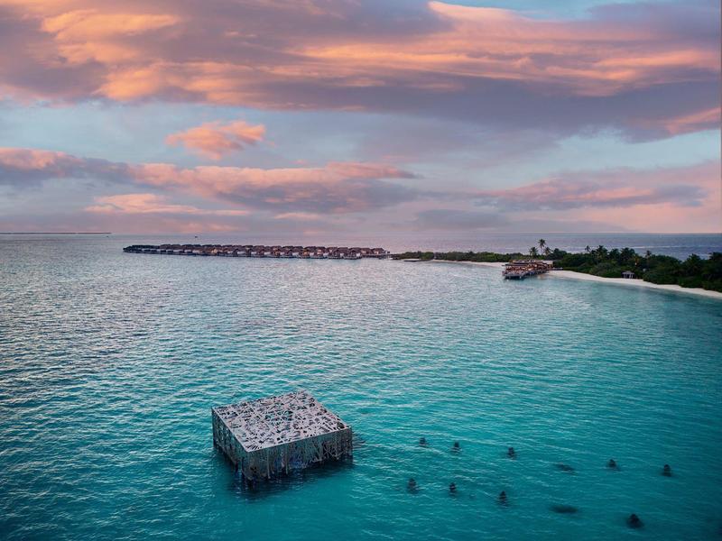 Strand mit klarem blauem Wasser, betoniertem Quadrat im Wasser und farbigem Abendhimmel.