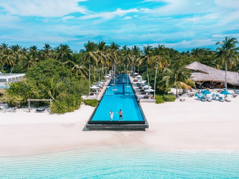 Weißer Sandstrand mit Pool, Palmen und blauem Himmel am tropischen Resort.
