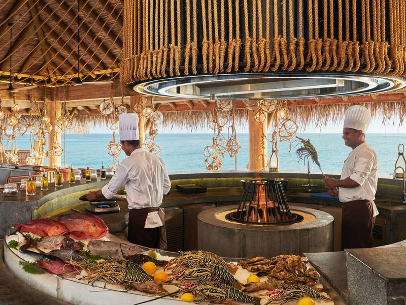 Offenes Fischrestaurant mit rustikalem Holzdesign, Grillfeuer in der Mitte und Köchen in weißen Uniformen.