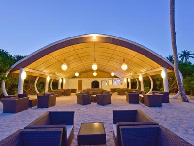Offener, moderner Strandpavillon mit sanfter Beleuchtung und gemütlichen Sitzbereichen in warmen Tönen.