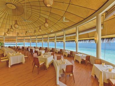 Elegantes Restaurant mit Holzboden und Meerblick, gedeckte Tische und stilvolle Beleuchtung.
