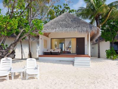 Bungalow sulla spiaggia con tetto di paglia, terrazza e due sedie a sdraio sulla sabbia.