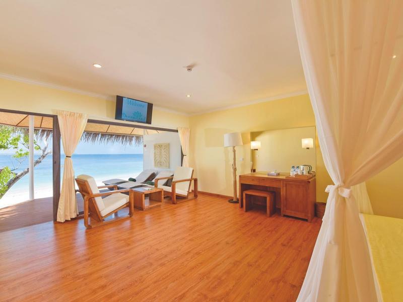 Heller Hotelraum mit Holzboden, Sitzecke, TV und Blick aufs Meer.