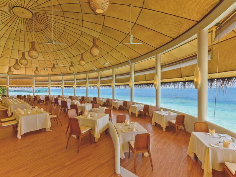 Offenes Restaurant mit gedeckten Tischen und Blick auf das Meer bei klarem Wetter.