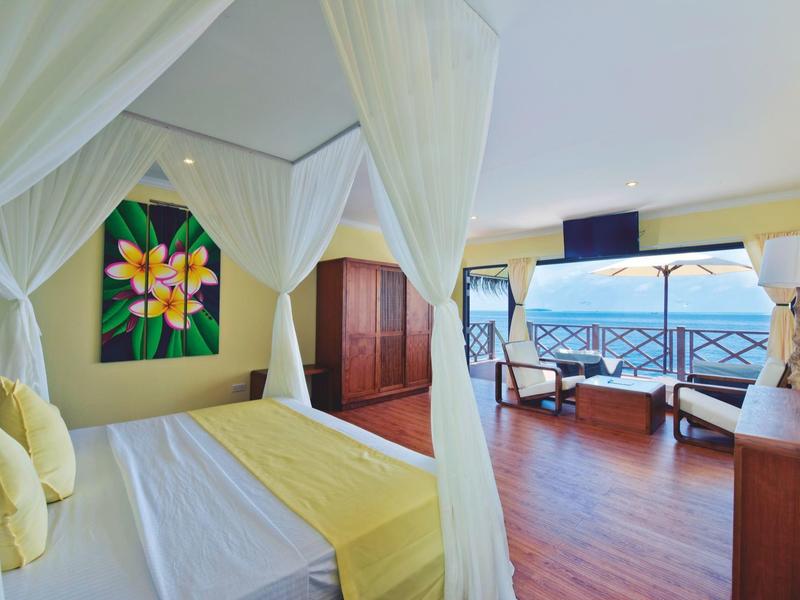 Helles Hotelzimmer mit Himmelbett, Holzfußboden und Balkon mit Meerblick.