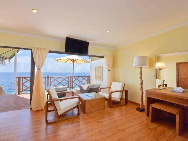 Helles Hotelzimmer mit Holzboden, Sitzbereich, Schreibtisch und Blick auf das Meer und Balkon.