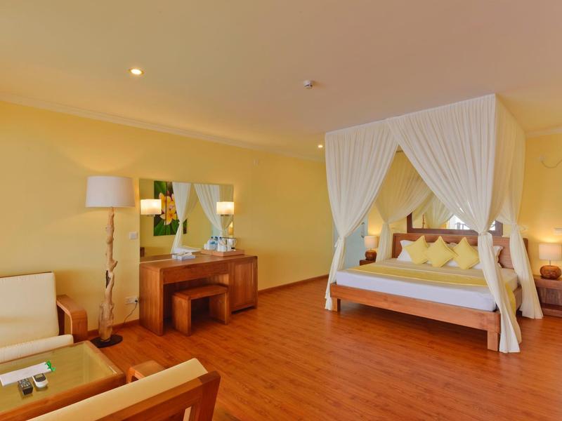 Hell eingerichtetes Hotelzimmer mit Himmelbett, Holzboden und Sitzbereich mit Sofa und Stühlen.