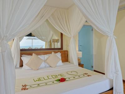 Schlafzimmer mit Himmelbett, weißen Vorhängen, Kissen und einem dekorativen "Welcome"-Schriftzug auf der Decke.