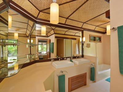 Helles Badezimmer mit großen Spiegeln, beige Fliesen, Holzakzenten und modernen Beleuchtungselementen.