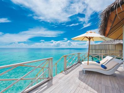 Hölzerne Terrasse mit Liegestühlen und Sonnenschirm am klaren türkisfarbenen Meer unter blauem Himmel.