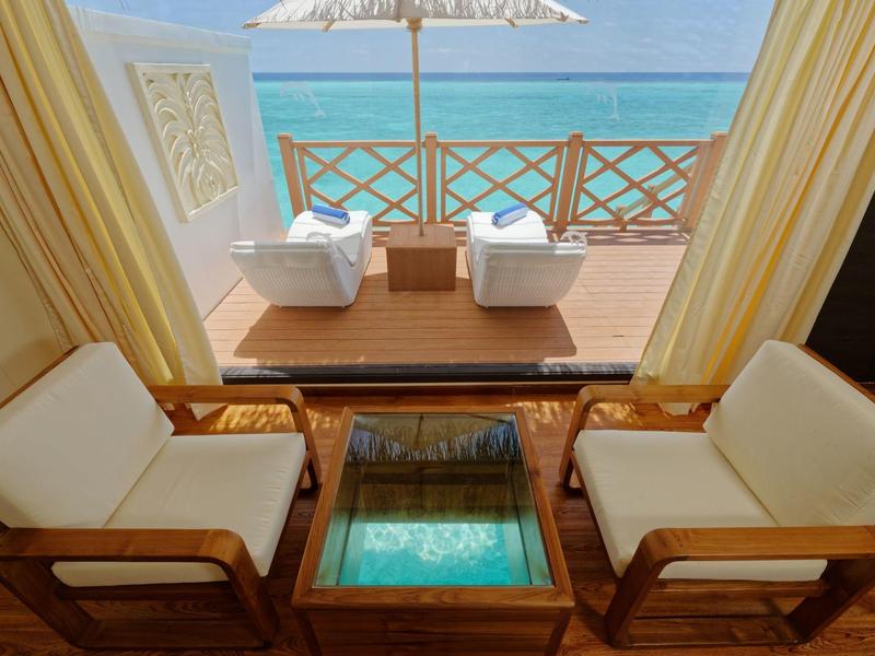 Einhellige Holzstühle mit weißen Kissen, Tisch mit Glasplatte, Blick auf Terrasse und Meer im Hintergrund.