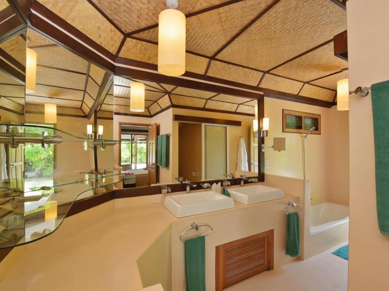 Helles Badezimmer mit großen Spiegeln, beige Fliesen, Holzakzenten und modernen Beleuchtungselementen.