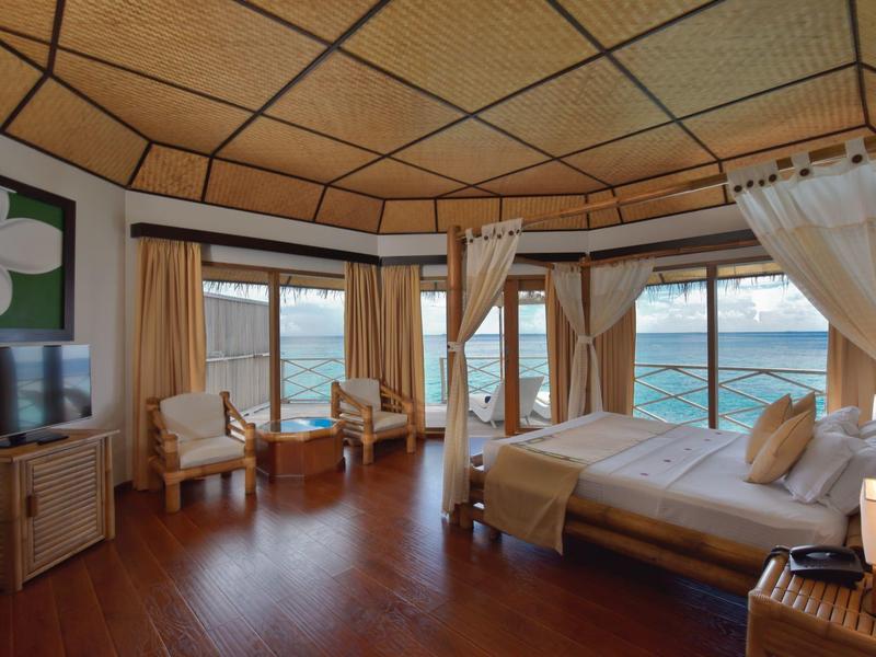 Großes Holzschlafzimmer mit Meerblick, Vorhängen, Sesseln, Fernseher und Himmelbett.