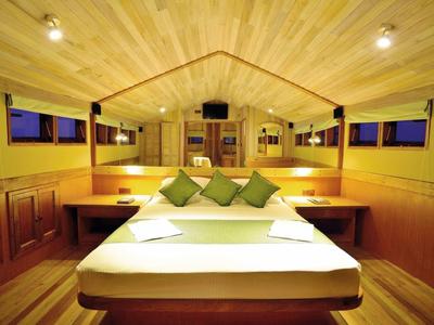 Gemütliches Holzschlafzimmer mit großem Bett, grünen Kissen und gedämpfter Beleuchtung.