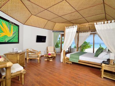 Geräumiges Schlafzimmer mit Holzfußboden, Himmelbett, buntem Wandbild und Blick auf tropische Natur.