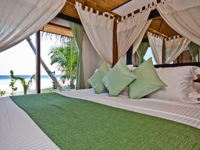 Helles Schlafzimmer mit großem Bett, weiß-grüner Bettwäsche, Moskitonetz und Meerblick.