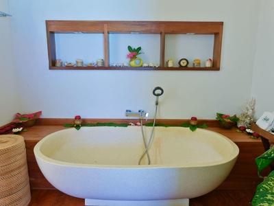 Moderner weißer freistehender Badewanne vor Holzregal mit Pflanzen und Dekoration.