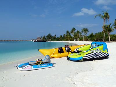 Weißer Sandstrand mit bunten Kajaks und Palmen vor türkisblauem Meer und blauem Himmel.