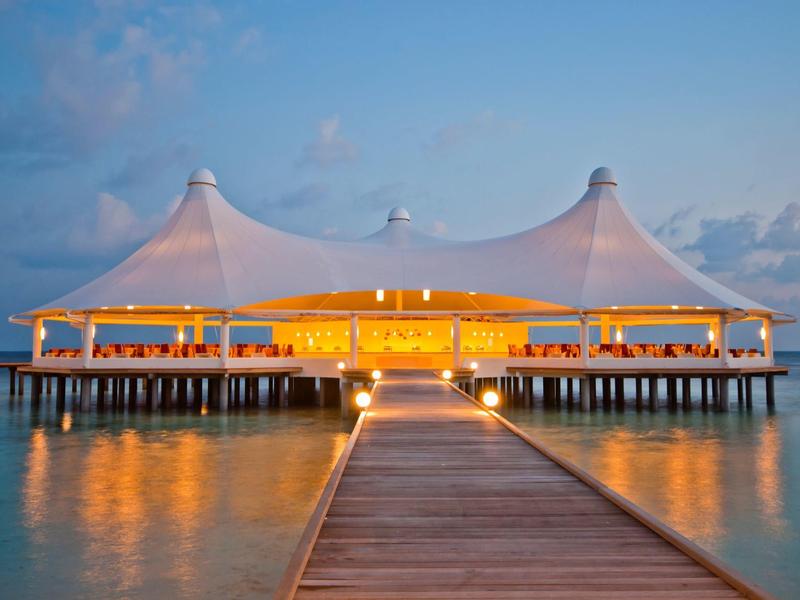 Beleuchtetes Restaurant auf einer Seebrücke bei Dämmerung über ruhigem Wasser.