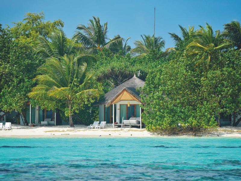 Strandresort mit weißem Sand, grünen Palmen und klarem blauem Wasser.