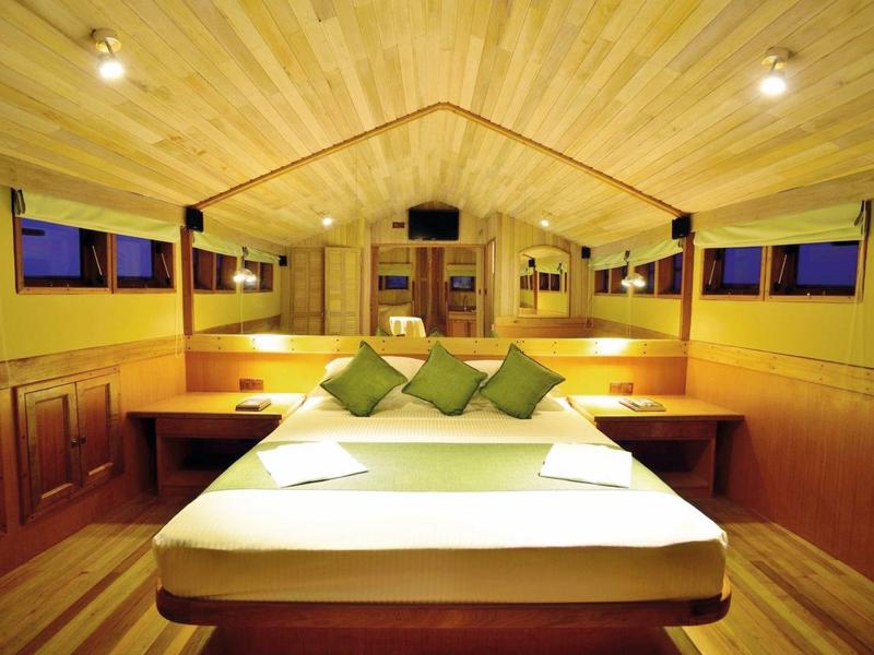 Gemütliche hölzerne Kabine mit großem Bett und grünen Kissen, sanft beleuchtet.