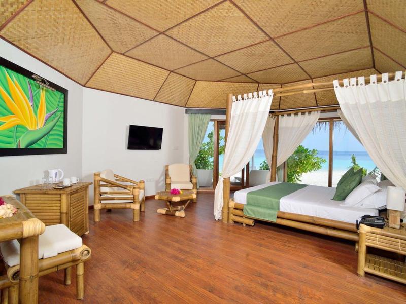 Geräumiges Hotelzimmer mit Holzdecke, Bett mit weißen Vorhängen und Blick auf das Meer.