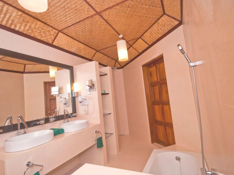 Helles Badezimmer mit Holztür, weißem Waschbecken, Badewanne und Spiegel unter einer Holzdecke.