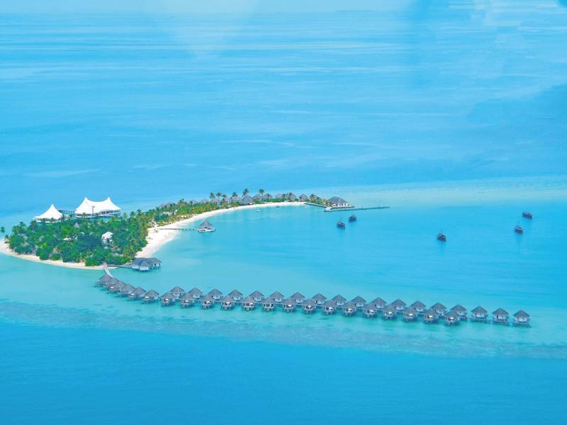 Luftaufnahme einer tropischen Insel mit über dem Wasser gebauten Bungalows und klarem blauem Meer.