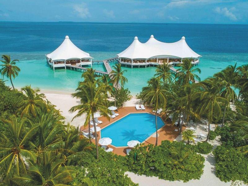 Weißes Strandresort mit Pool, Palmen und Zeltdächern am türkisfarbenen Meer.