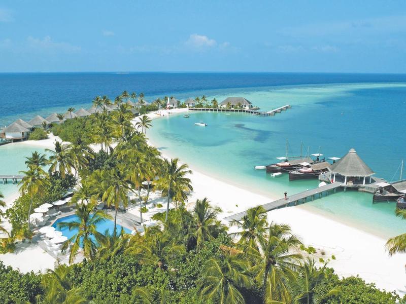 Tropische Insel mit weißen Sandstränden, Palmen und blauem Meer vor klarem Himmel.