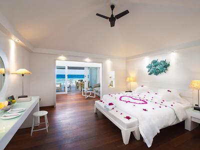 Helles Schlafzimmer mit weißem Doppelbett, Holzboden, Deckenventilator und Balkon mit Meerblick.