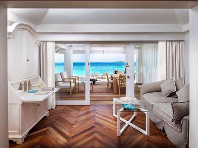Helles Wohnzimmer mit braunem Parkett, grauem Sofa, weißem Sekretär und Meerblick durch Glasfront.