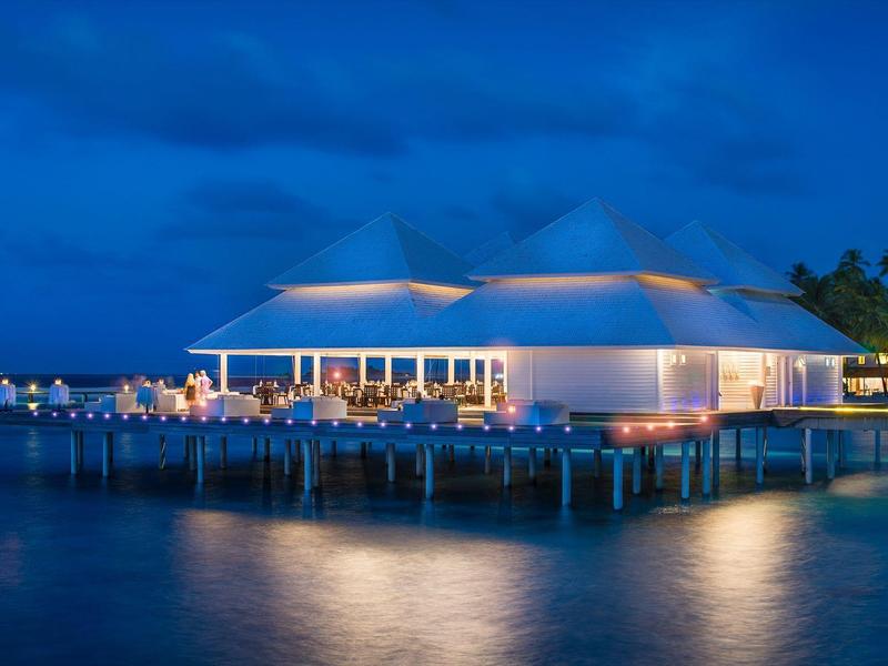 Beleuchtetes Restaurant auf Stelzen über dem Wasser bei Nacht.