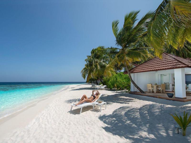Weißer Sandstrand mit Palmen, Liegestühlen und einem kleinen Häuschen am Meer.