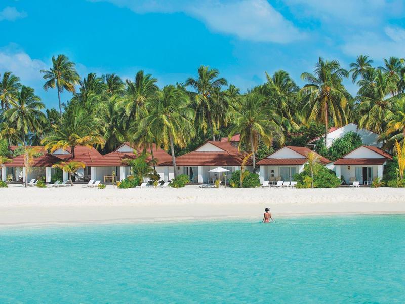 Strandbungalows mit Palmen und klarem türkisfarbenem Wasser bei sonnigem Himmel