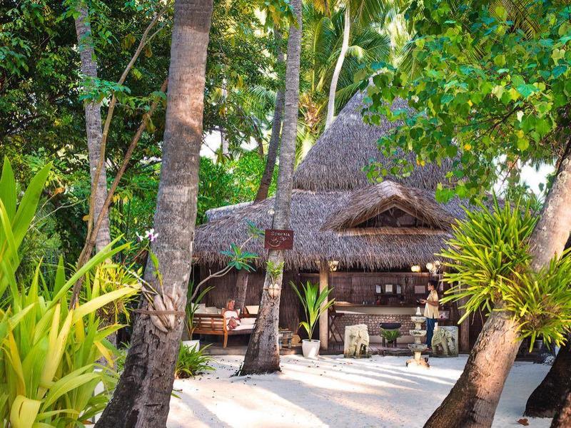 Ein balinesisches Gartenhaus mit Strohdach umgeben von tropischen Pflanzen und Palmen.